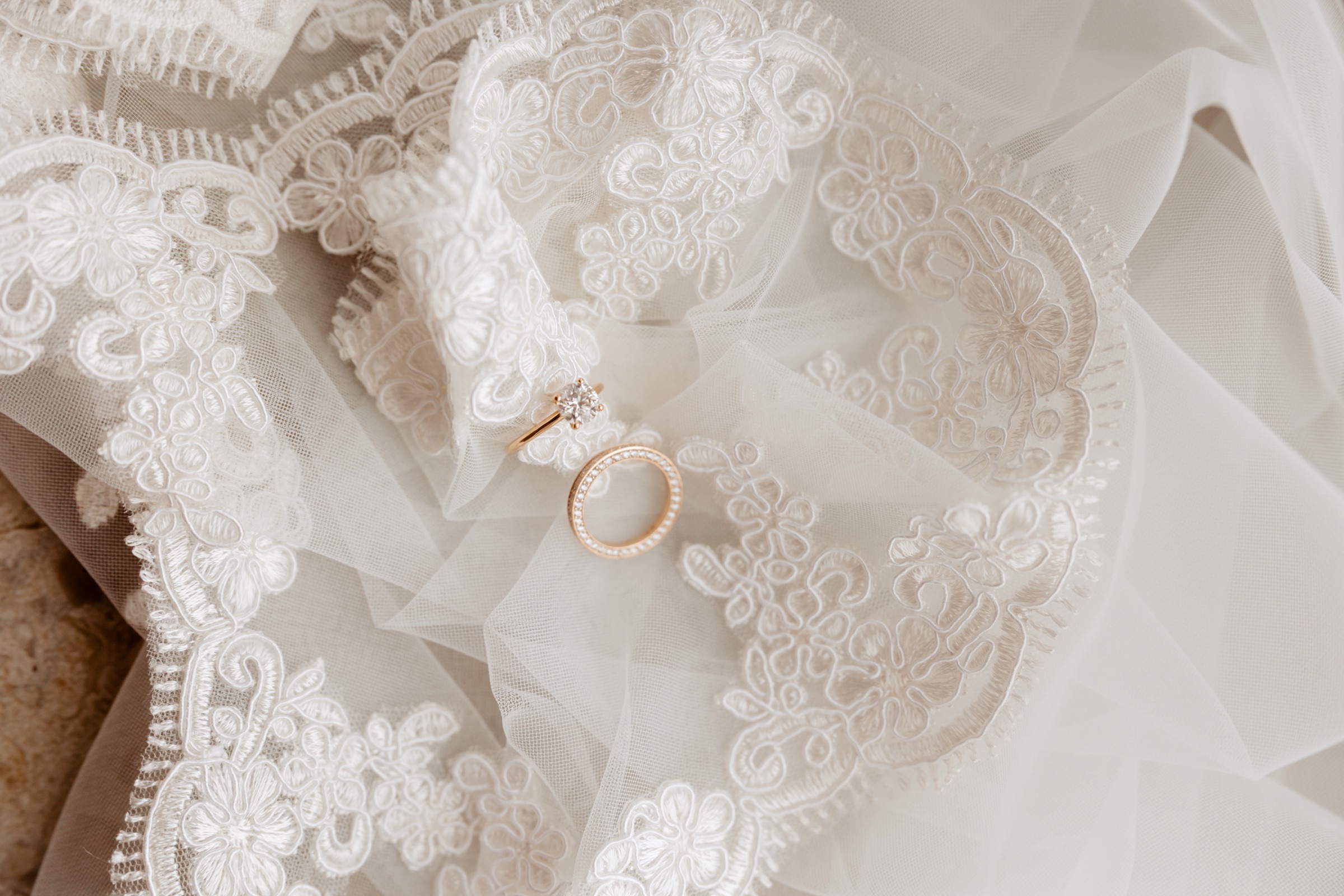 A pair of wedding rings resting on bridal lace in soft atelier light